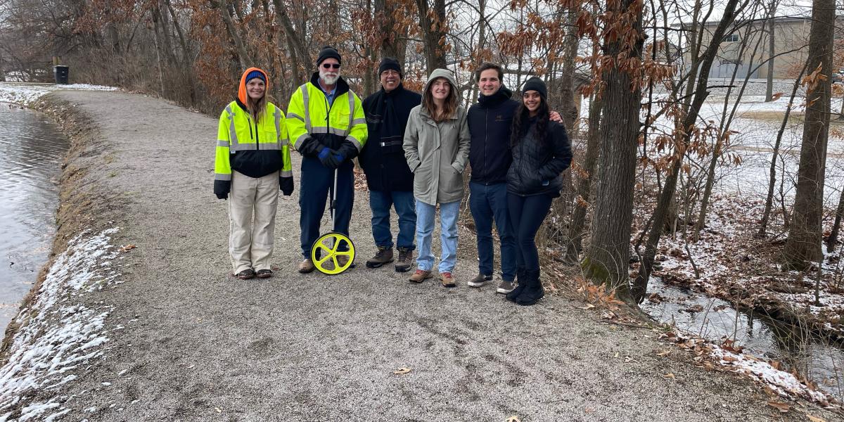 Six people stand side by side on a dirt road, smiling at the camera.