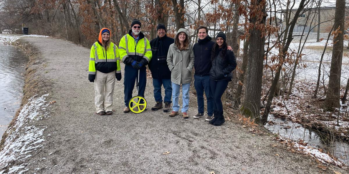 Six people stand side by side on a dirt road, smiling at the camera.