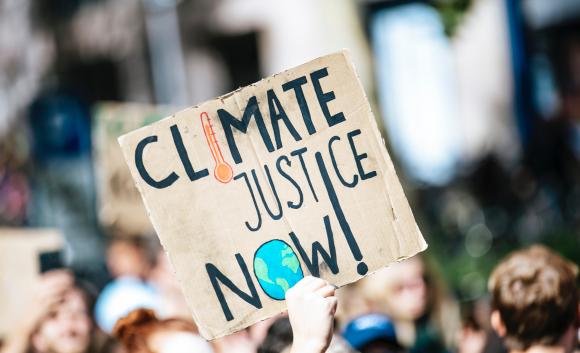 person holding sign that reads "climate justice now" at a rally